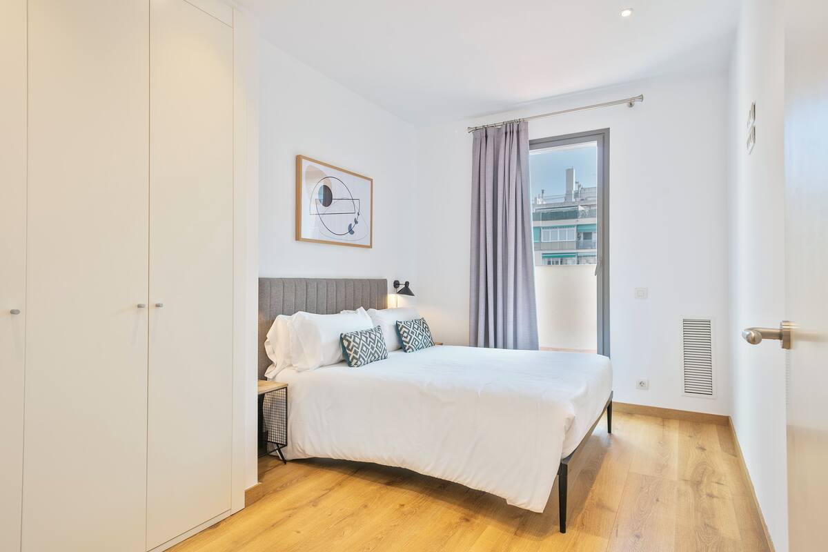 Une chambre moderne avec un grand lit, une tête de lit, une table de chevet, une fenêtre avec des rideaux et une vue sur la ville.