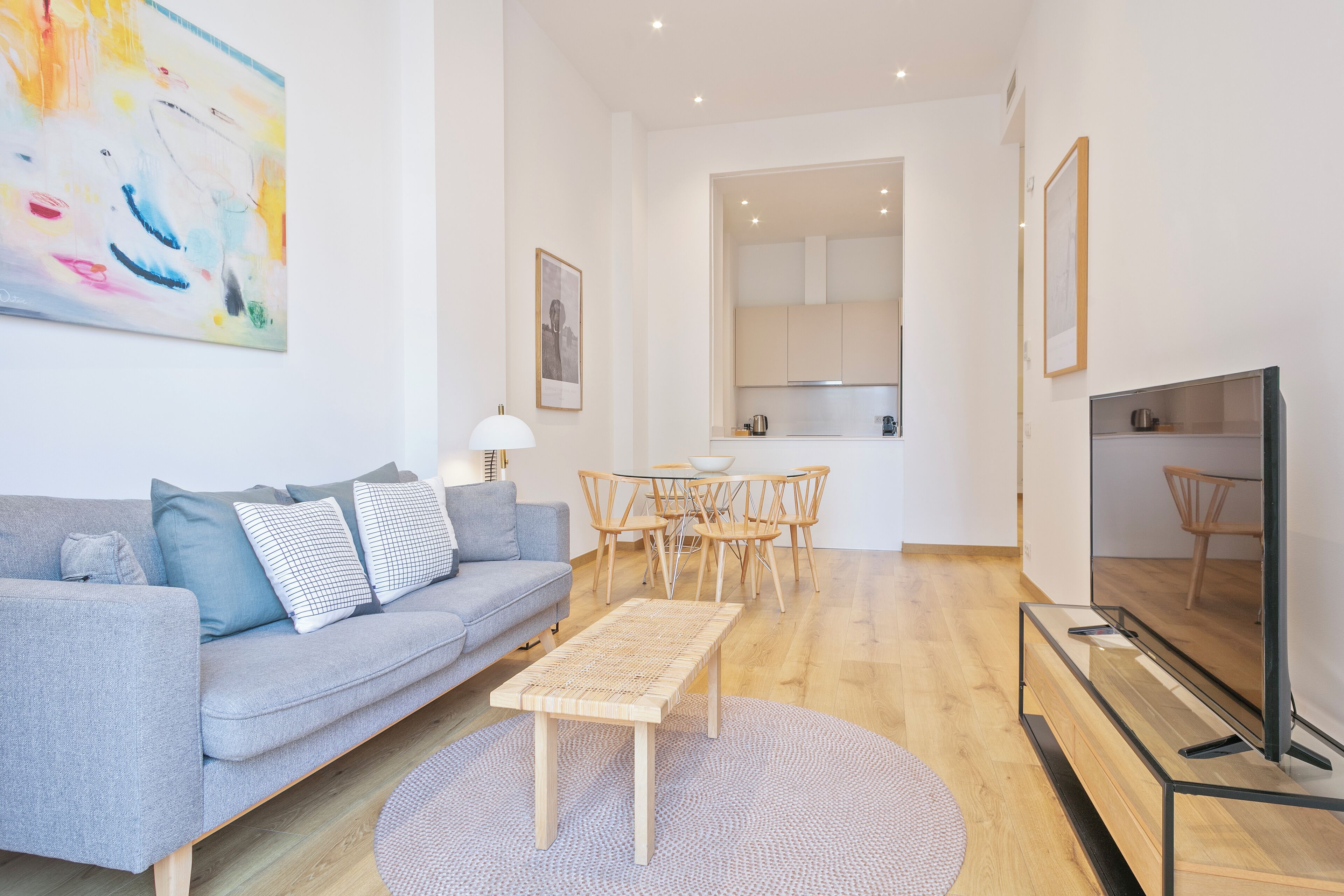 Een moderne woonkamer met een grijze bank, een houten salontafel en een televisie op een dressoir.