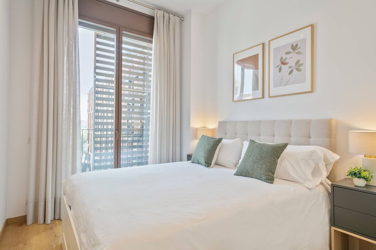 Une chambre d’hôtel avec un grand lit, une table de chevet avec une lampe et une fenêtre avec des rideaux.