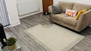 A living room with a sofa, a coffee table, a potted plant, and a radiator. - Chaucer House Retreat - Leicester (Leicester)
