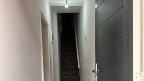 A narrow hallway with a dark wooden floor, white walls, and a closed dark wooden door on the right. A white radiator is visible on the left wall. - Chaucer House Retreat - Leicester (Leicester)