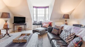 A loft-style living room with a television, seating area, and a view through a large window.