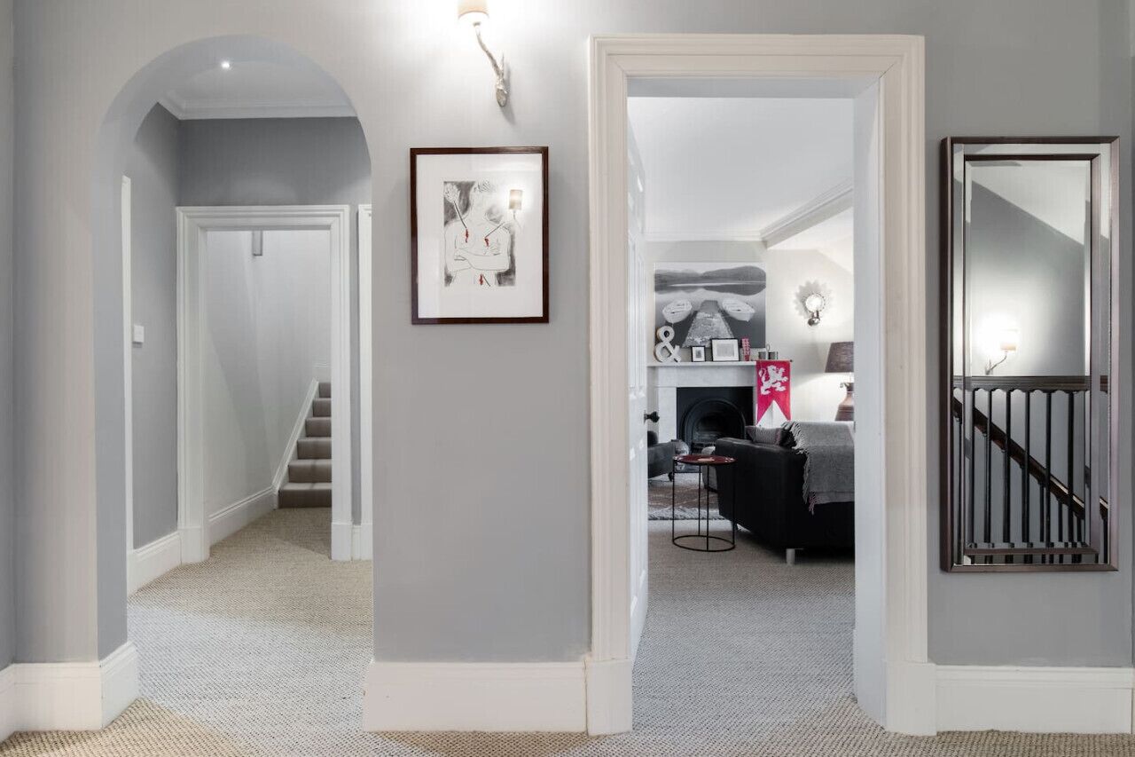A hallway with a staircase, a framed picture, a fireplace, and a mirror.
