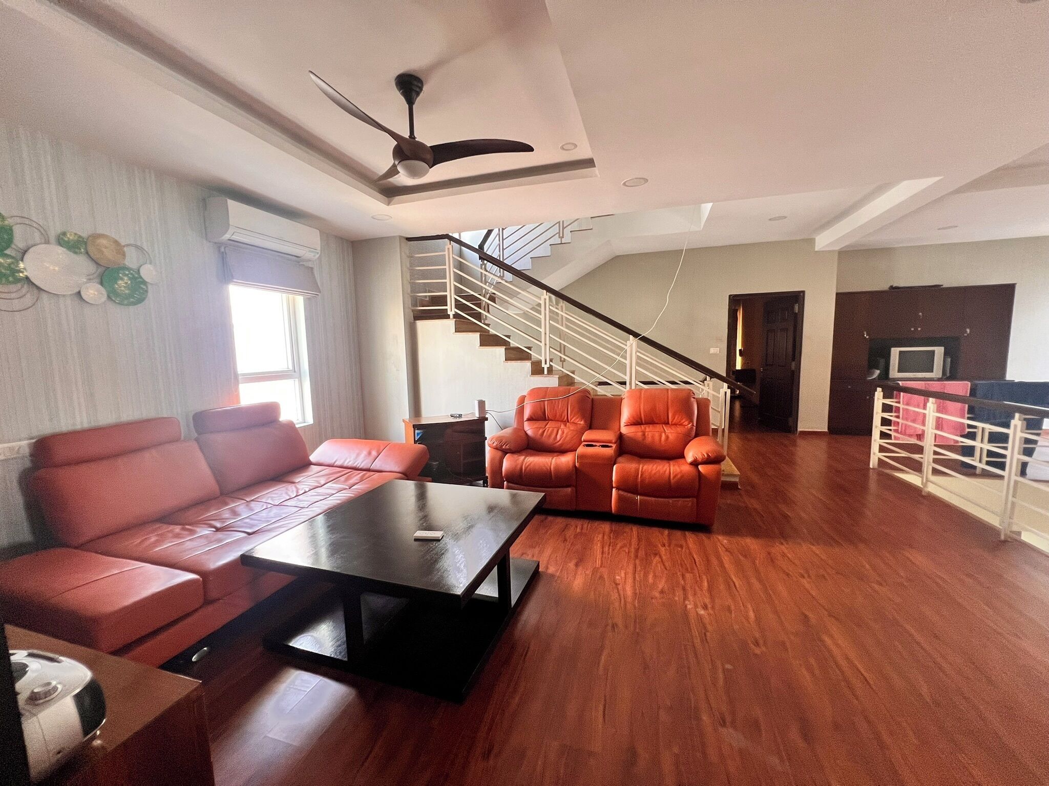 A spacious living area with a sofa, a recliner, a coffee table, and a staircase leading to an upper floor.