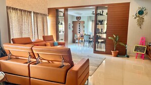 A spacious living area with a modern orange sofa, a dining table with chairs, a potted plant, and a chalkboard on a stand.