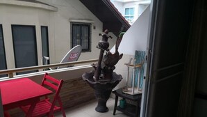 A balcony with a red table and chairs, a decorative fountain, and a UBC sign. - Room in Apartment - Jomtien Hill Resort Pratamnak 105 (Pattaya)