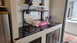 A kitchen with a black countertop, a sink, and cabinets. There is a dish rack, a roll of paper towels, and a pink dish rack on the counter. - Room in Apartment - Jomtien Hill Resort Pratamnak 105 (Pattaya)
