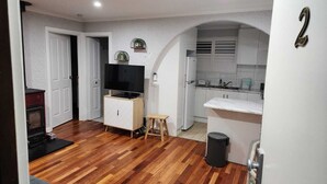 A compact living space with a kitchen, a television on a wooden cabinet, a small stool, and a trash bin. - 2BDR Holiday Flat near Bright-Entire Place (Freeburgh)