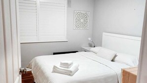 A neatly arranged bedroom with a bed, a bedside table, a lamp, and a window with blinds. - 2BDR Holiday Flat near Bright-Entire Place (Freeburgh)