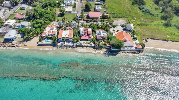 Vista aérea de una zona residencial costera con casas, una playa y aguas turquesas cristalinas.
