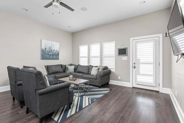 A modern living room with a sectional sofa, a coffee table, and a flat-screen TV mounted on the wall. - Urban Retreat | Walkable | Easy Parking | Spacious (Indianapolis)