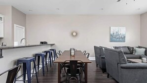 Une cuisine moderne avec un îlot central, un coin repas avec une longue table et des chaises, et un canapé gris dans l’espace salon.