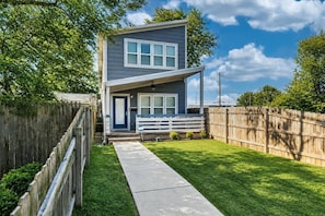 A two-story house with a front porch, a wooden fence, and a well-maintained lawn. - Urban Retreat | Walkable | Easy Parking | Spacious (Indianapolis)