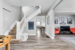 A spacious living area with a wooden floor, a staircase, a dining area, and a television. - 4BR Family Retreat | Ideal Location | Sleeps 15! (Indianapolis)