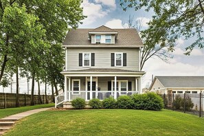 A two-story house with a front porch, a small attached garage, and a fenced yard. - 4BR Family Retreat | Ideal Location | Sleeps 15! (Indianapolis)