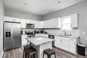 A modern kitchen with white cabinets, stainless steel appliances, a marble countertop island, and a wooden floor. - 4BR Family Retreat | Ideal Location | Sleeps 15! (Indianapolis)