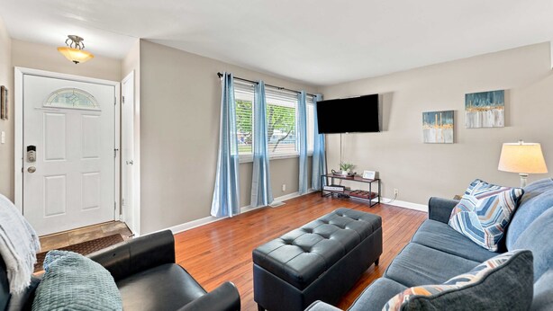Uma sala de estar com sofá, apoio para os pés e uma TV de tela plana fixada na parede.