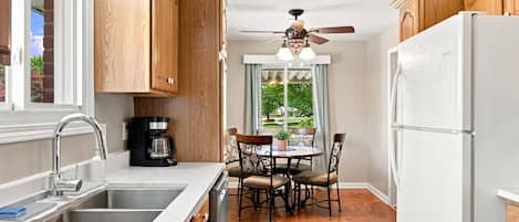 A kitchen with wooden cabinets, a white refrigerator, a coffee maker, a dining table with chairs, and a ceiling fan.