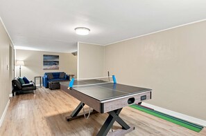 A ping pong table in a room with a sofa, lamp, and a painting on the wall. - Beech Grove Retreat | Private Yard • Game Floor! (Beech Grove)