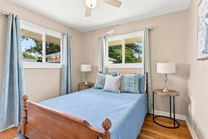 A bedroom with a wooden bed, two bedside tables with lamps, a ceiling fan, and windows with curtains. - Beech Grove Retreat | Private Yard • Game Floor! (Beech Grove)
