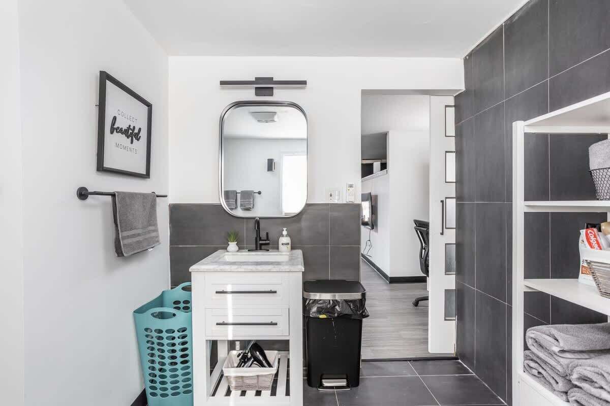 A modern bathroom with a white vanity, a large mirror, a towel rack, and a trash bin.