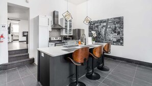 Une cuisine moderne avec un îlot central, des tabourets de bar et une œuvre d’art représentant un paysage urbain accrochée au mur.