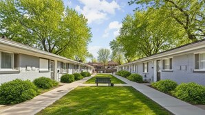 Une rangée de bâtiments d’un seul étage, typiques des motels, avec une pelouse centrale et un banc.