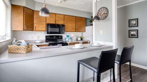 Une cuisine moderne avec des meubles en bois, un îlot central, des chaises noires et des luminaires suspendus.