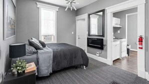 A modern bedroom with a grey color scheme, a bed with a grey duvet, a black bedside lamp, a small plant, and a framed picture on the nightstand. - New Castle Retreat | Beautiful Duplex • Near Parks (New Castle)