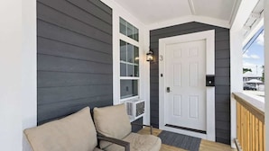 A porch with a beige chair, a white door, and a window with blinds. - New Castle Retreat | Beautiful Duplex • Near Parks (New Castle)