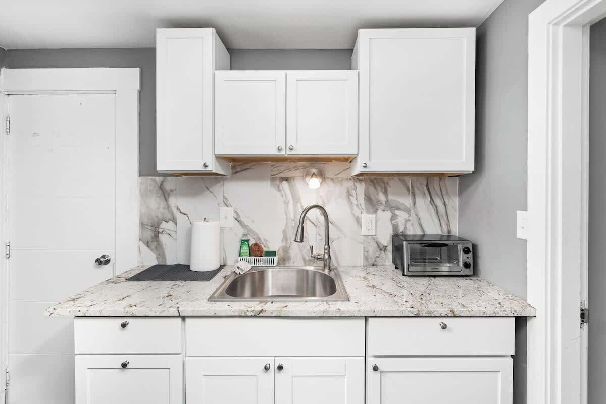 A kitchen with white cabinets, a marble countertop, a stainless steel sink, and a built-in toaster oven.