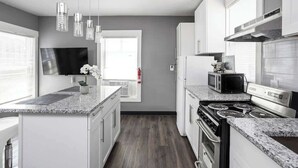 A modern kitchen with white cabinets, granite countertops, a stainless steel stove, and a flat-screen TV. - New Castle Getaway | Fireplace • Prime Location (New Castle)