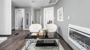 A modern living room with a glass coffee table, two white armchairs, a fireplace, and grey walls. - New Castle Getaway | Fireplace • Prime Location (New Castle)