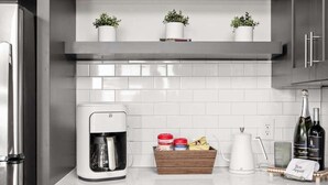 Une cuisine moderne avec des meubles de couleur sombre, une machine à café, une horloge et des objets décoratifs disposés sur des étagères.
