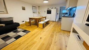 A compact living space with a sofa, a wooden dining table, a bench, and a kitchenette.