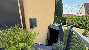 A welcome mat with text, a potted plant, a black outdoor heater, and a metal fence.