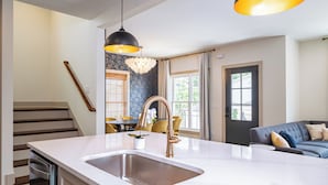 A modern kitchen with a large island, stainless steel sink, and a black pendant light.