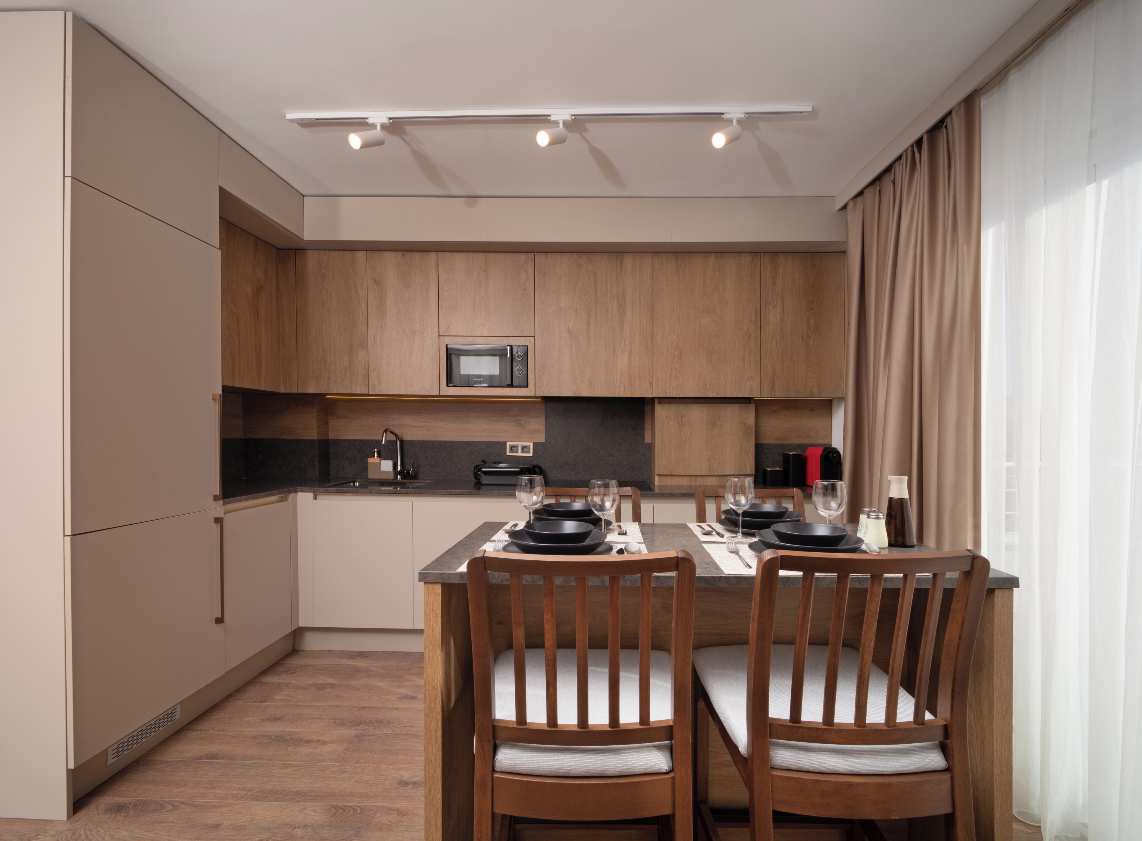 A modern kitchen with wooden cabinets, a microwave, and a dining area with two chairs and a table set for two.