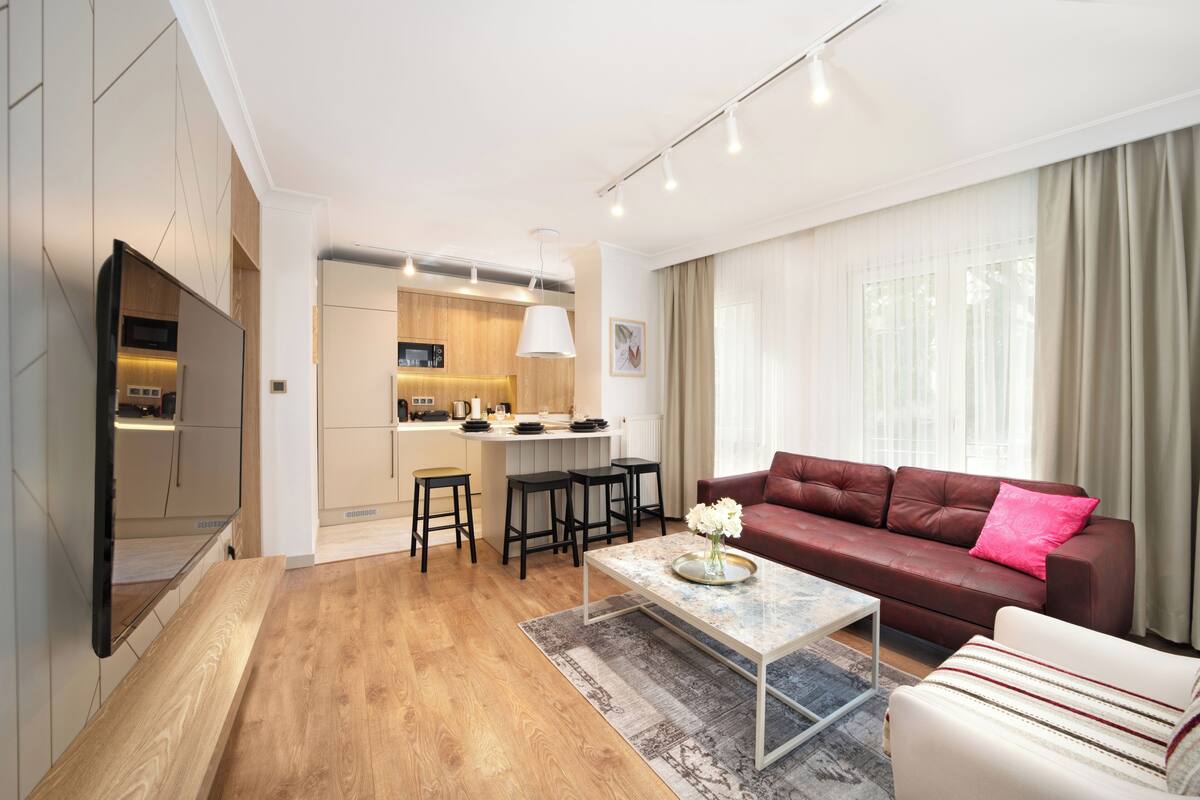 A modern living room with a brown leather sofa, a coffee table, and a kitchen area in the background.