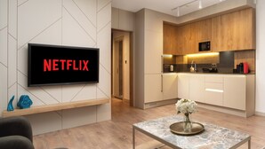 A modern living room with a flat-screen TV displaying "NETFLIX", a kitchen with wooden cabinets, and a dining area with a marble table. - Marmada Suites (Istanbul)
