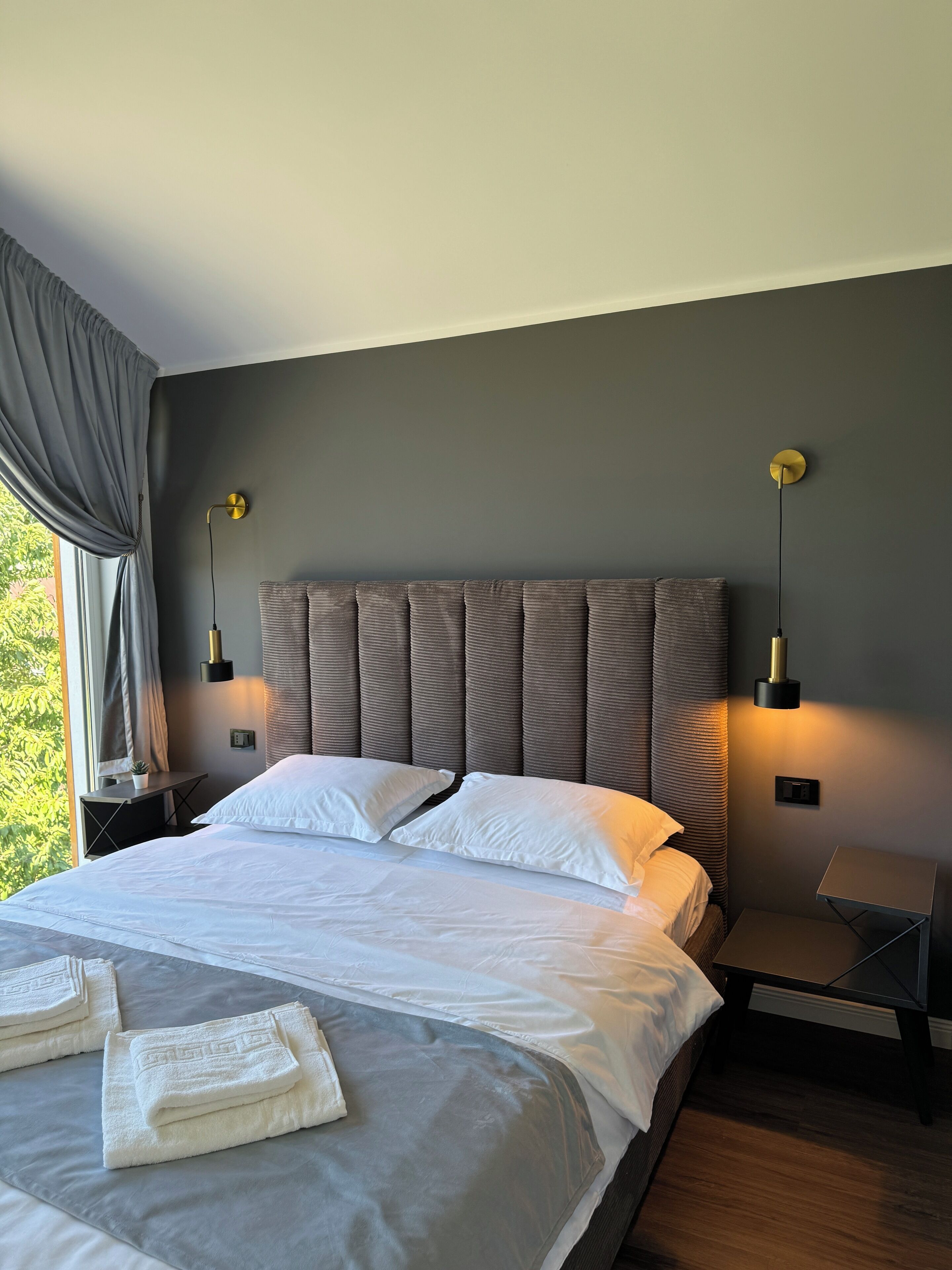 Un dormitorio moderno con una cama grande, paredes grises y una ventana con cortinas.