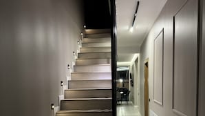 A modern staircase with a dark finish, leading to a well-lit hallway with a wooden door at the end.