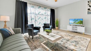 A modern living room with a sofa, two armchairs, a coffee table with a plant, a TV on a white cabinet, and a ceiling fan. - 3-bedroom townhome in delightful Kissimmee with WiFi, AC, and Cable TV. (Kissimmee)