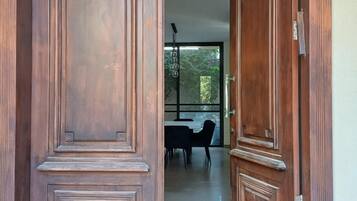 A wooden double door with a 'WELCOME' mat at the entrance, leading to a dining area with a table and chairs.