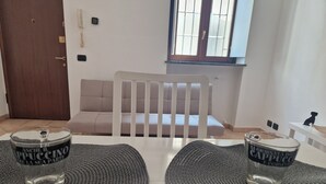 A room with a white sofa, a wooden door, a window with blinds, and two glasses on a woven placemat.