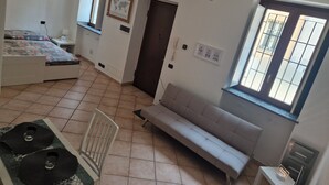 A bedroom with a bed, a sofa, a chair, a small table, and a window.