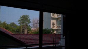 A view through a window with a red-tiled roof, a balcony railing, and a building with multiple air conditioning units and balconies in the background. - Jomtien Hill Resort Pratamnak 107 (Pattaya)