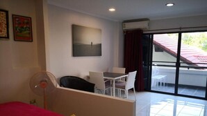A hotel room with a bed, a desk, a chair, a fan, and a balcony with a view of the outside. - Jomtien Hill Resort Pratamnak 107 (Pattaya)