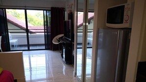 A hotel room with a bed, a TV, a refrigerator, and a sliding glass door leading to a balcony. - Jomtien Hill Resort Pratamnak 107 (Pattaya)