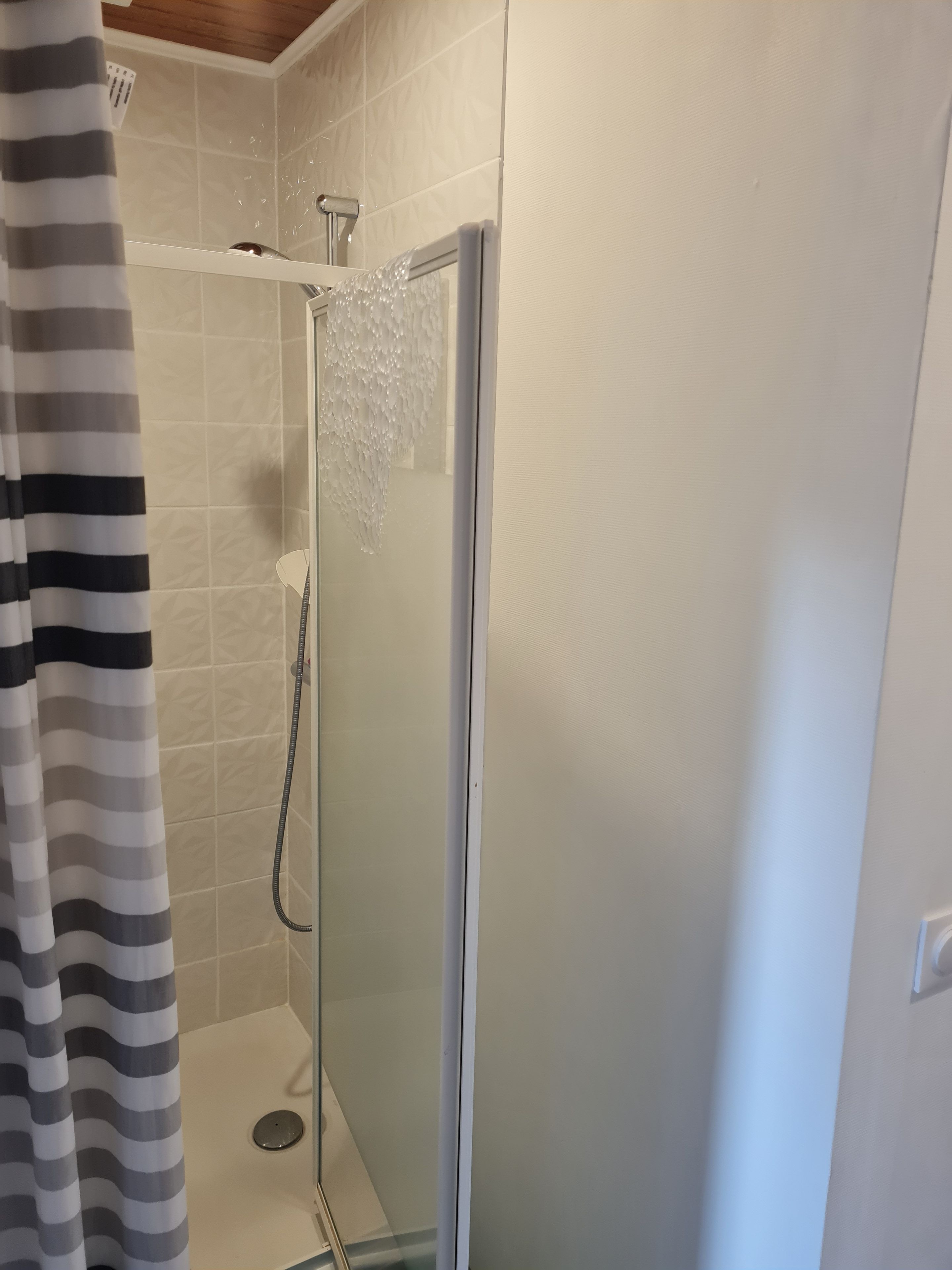 A shower enclosure with a frosted glass door, a handheld showerhead, and a shower control panel.